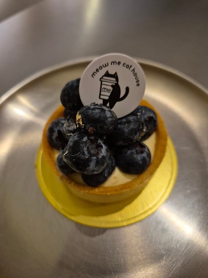 A blueberry tart topped with a round Meow Me Cat House tag
